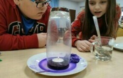Dwoje dzieci (chłopiec i dziewczynka) przyglądają się eksperymentowi z fioletową wodą i świeczką typu tea light 